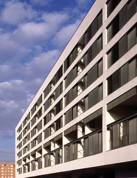 Edificio de apartamentos moderno de color blanco con balcones contra un cielo azul con nubes.