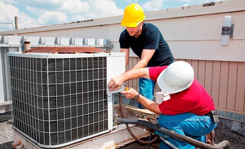 Dos trabajadores de climatización reparando una unidad de aire acondicionado exterior en una azotea.