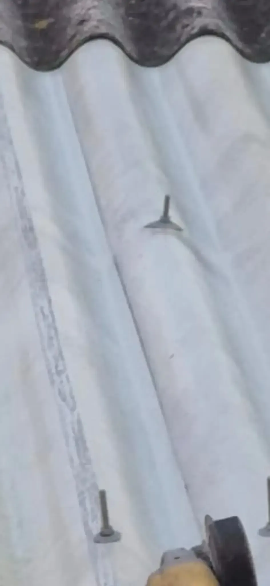 Primer plano de un techo blanco ondulado con dos tornillos a la vista y una pequeña zona dañada.