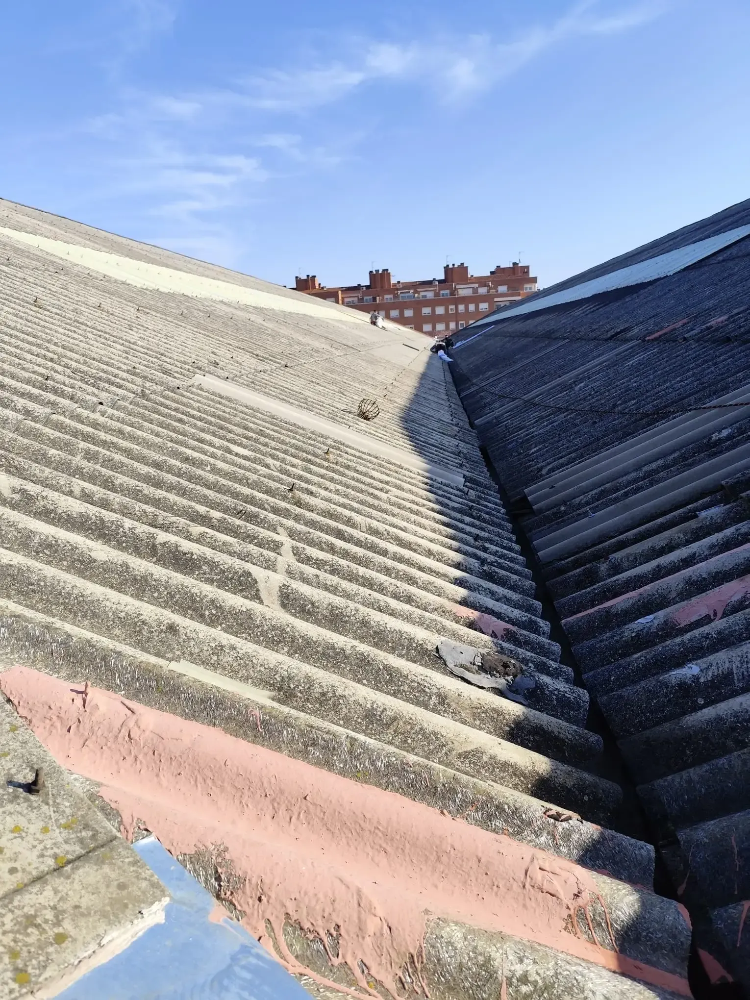 Tejado de chapa ondulada desgastada con cumbrera, visto desde abajo bajo un cielo azul