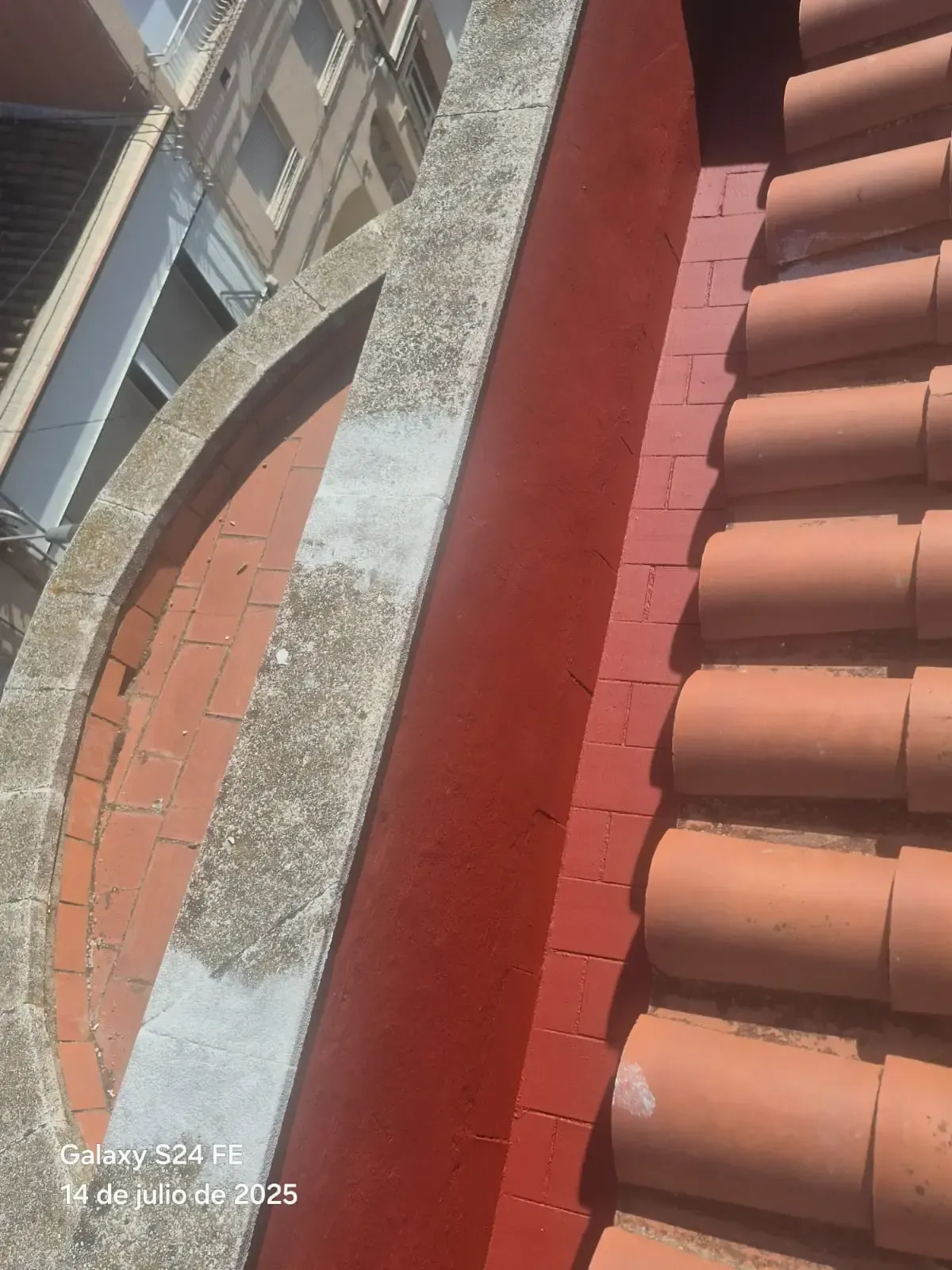 Azotea con tejas rojas, pared de ladrillo y canalón de hormigón arqueado junto a un edificio