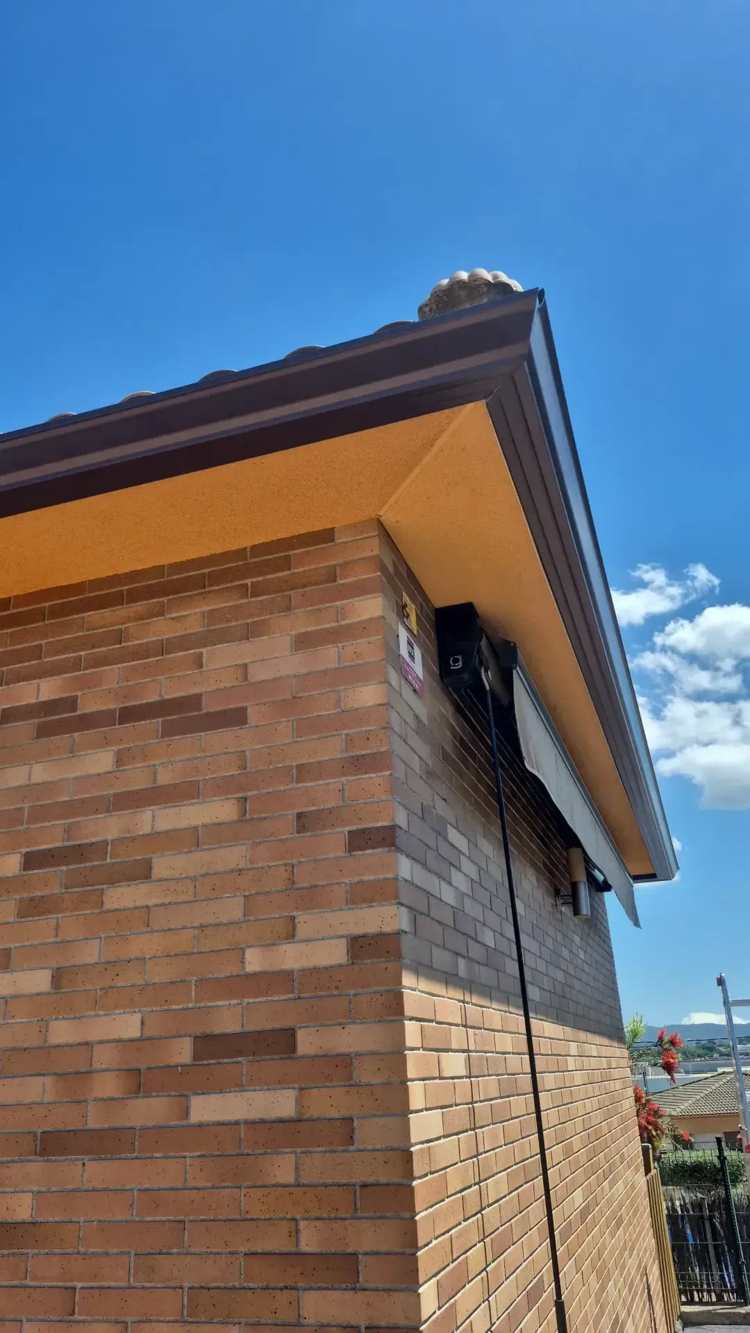 Esquina de un edificio de ladrillo con el borde oscuro del tejado recortado contra un cielo azul con nubes