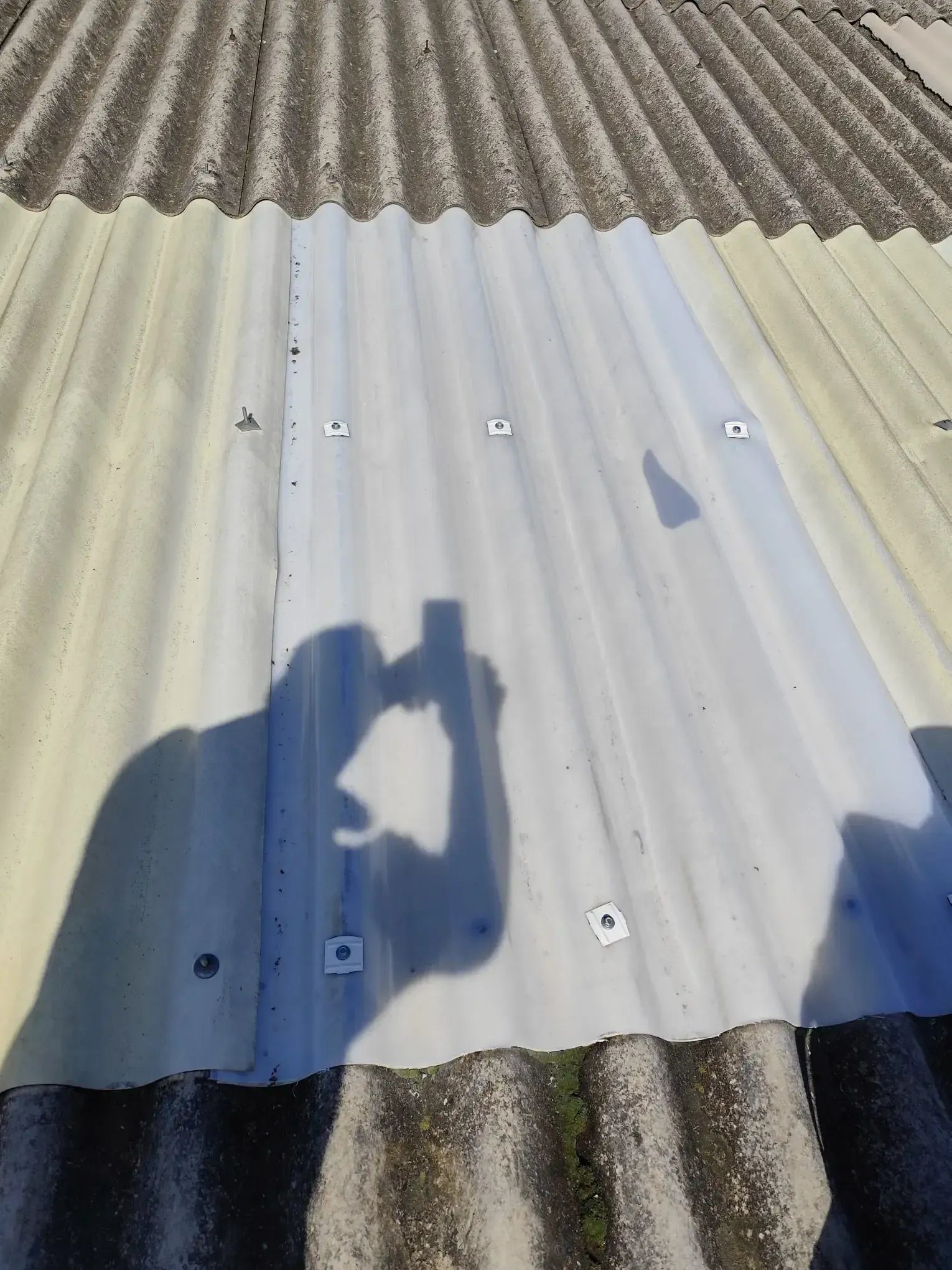 Panel de techo corrugado blanco con tornillos y la sombra de una persona haciendo la foto