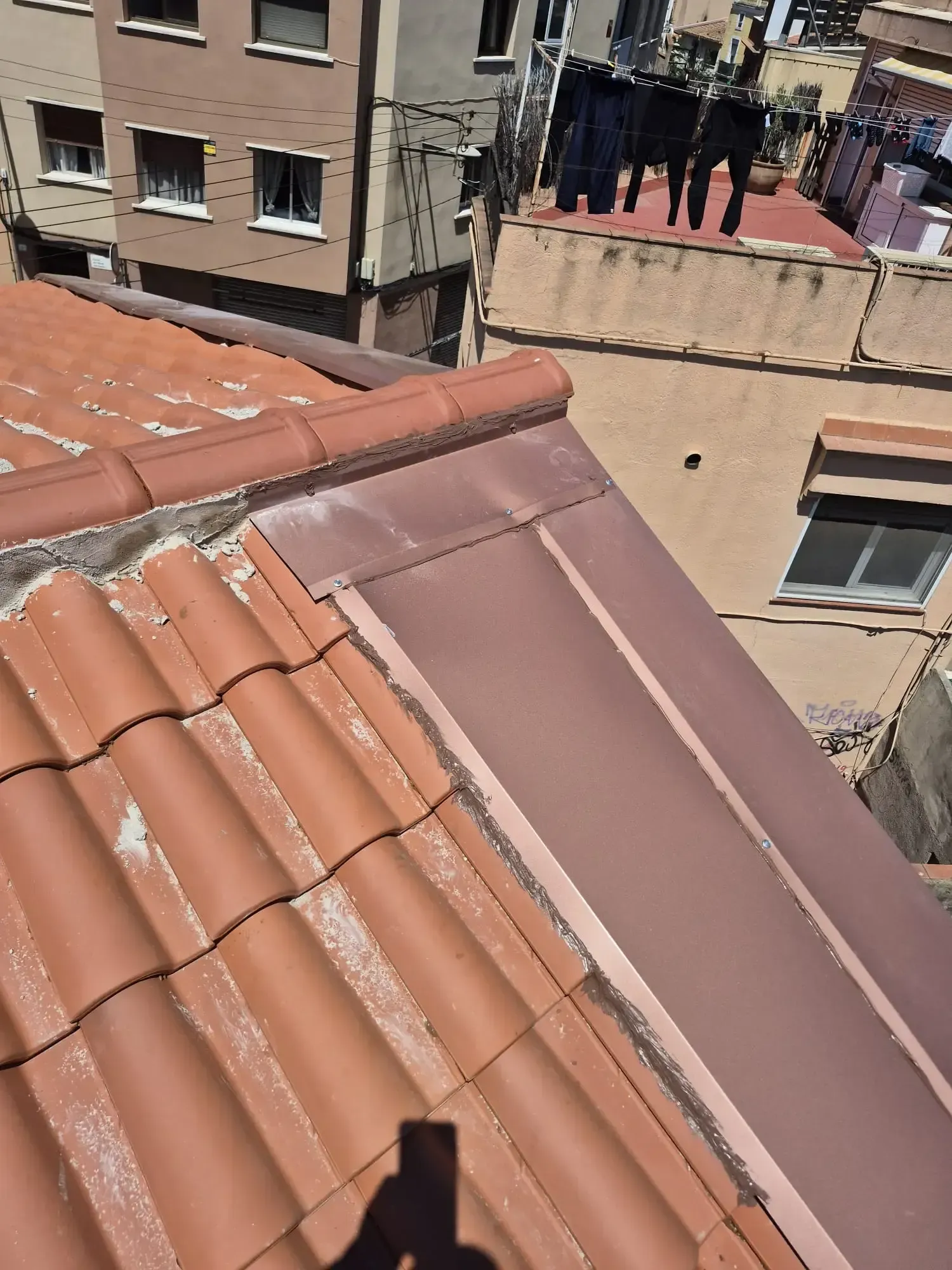 Vista desde una azotea de tejas de terracota y el balcón de un edificio cercano, con gente de pie en el exterior