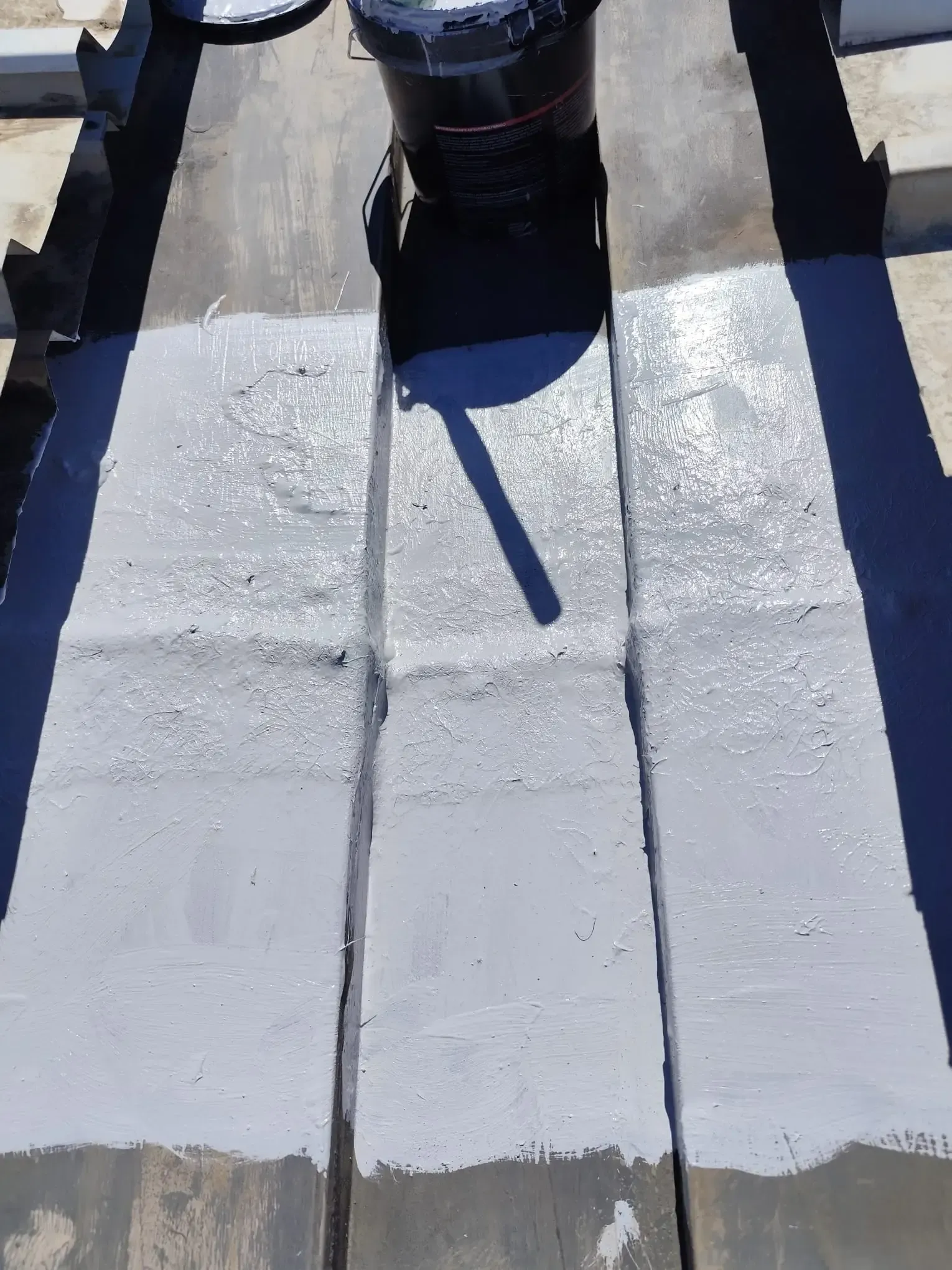 Pasarela de azotea pintada de blanco, con una tubería negra y una larga sombra que la cruza por el centro