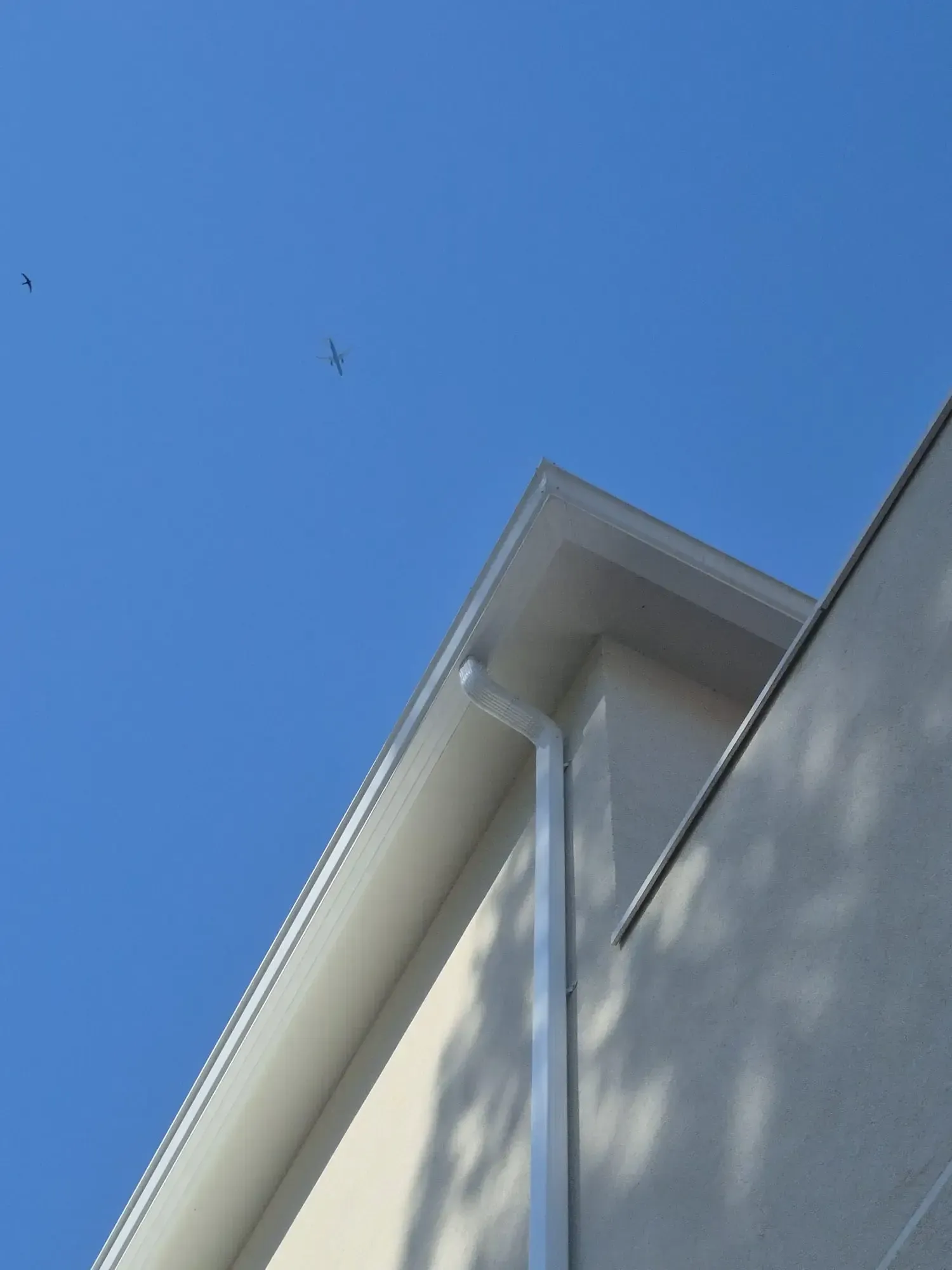 Cielo azul sobre el tejado de una casa, con canalones blancos y un bajante en la esquina