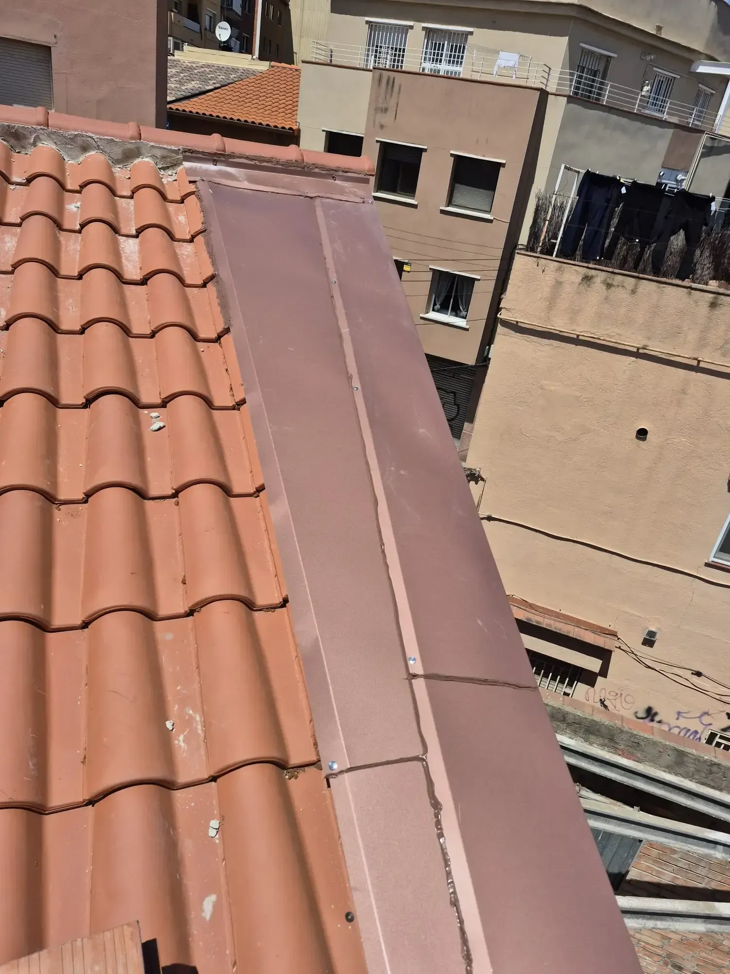 Tejados de tejas rojas y un techo de metal marrón junto a edificios de apartamentos beige bajo un sol radiante