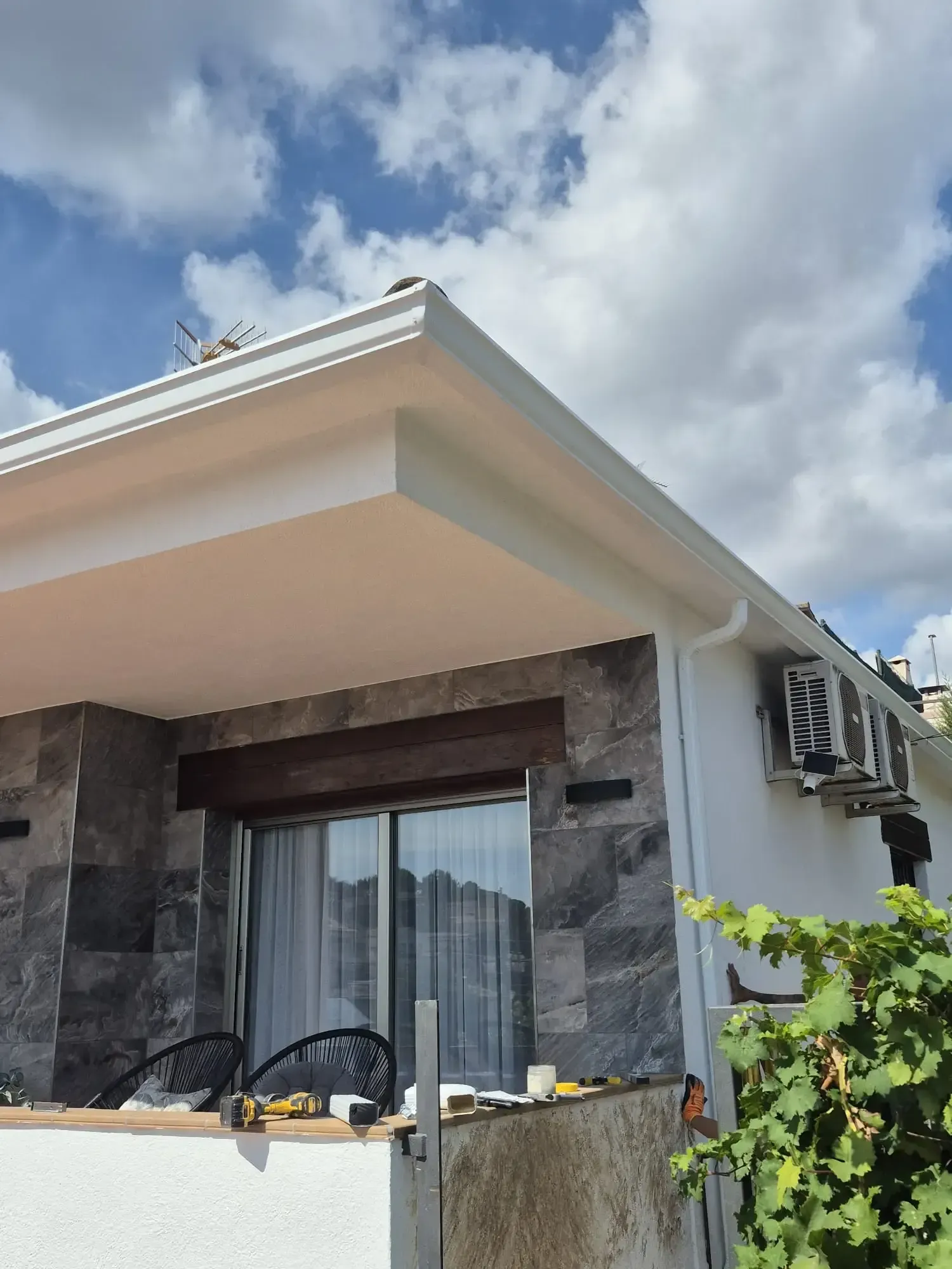 Exterior de una casa moderna con fachada de piedra, balcón, alero blanco y cielo nublado
