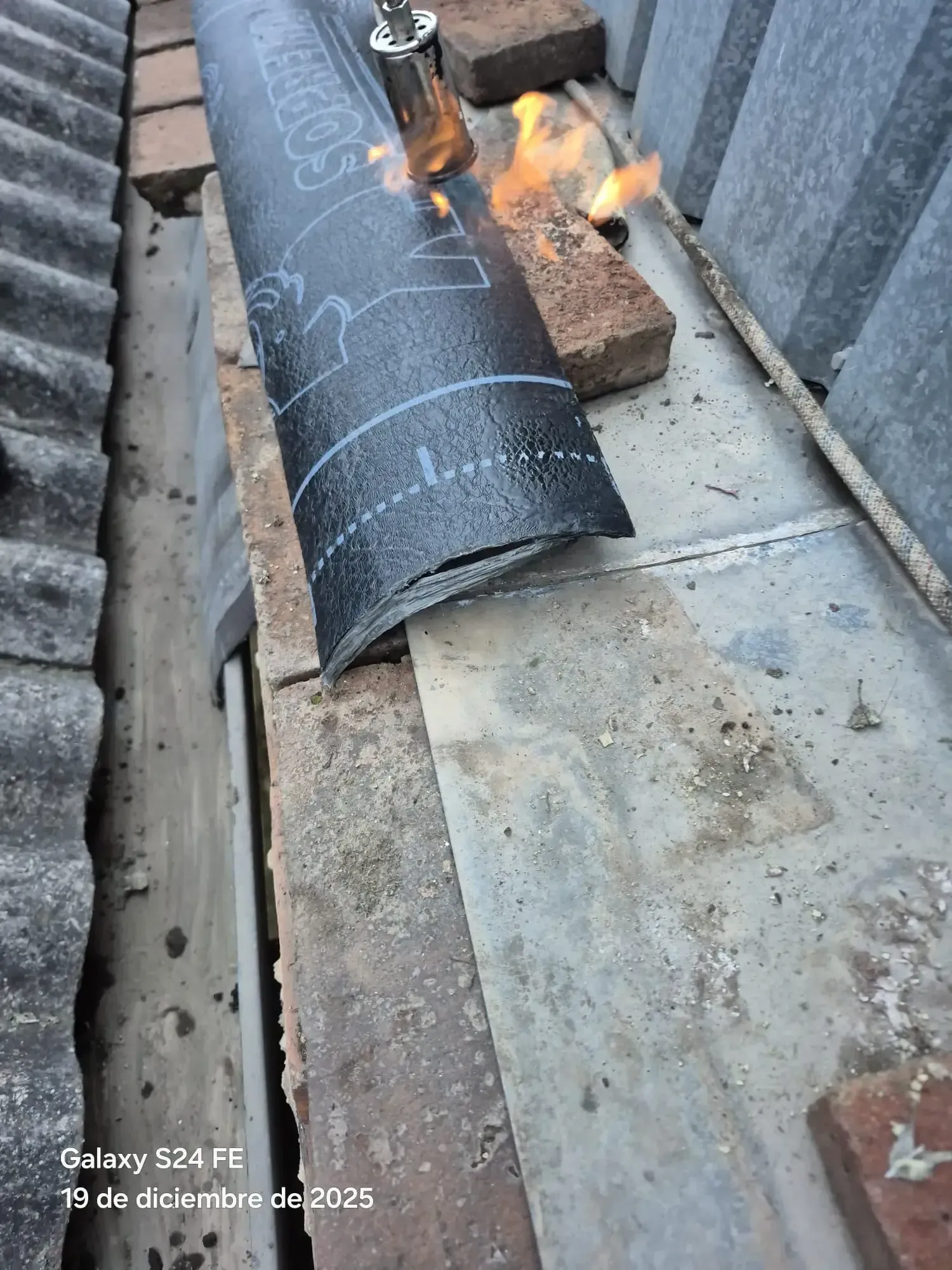 Calentando con soplete un material negro para techos, sobre una azotea junto a ladrillos y losas de hormigón