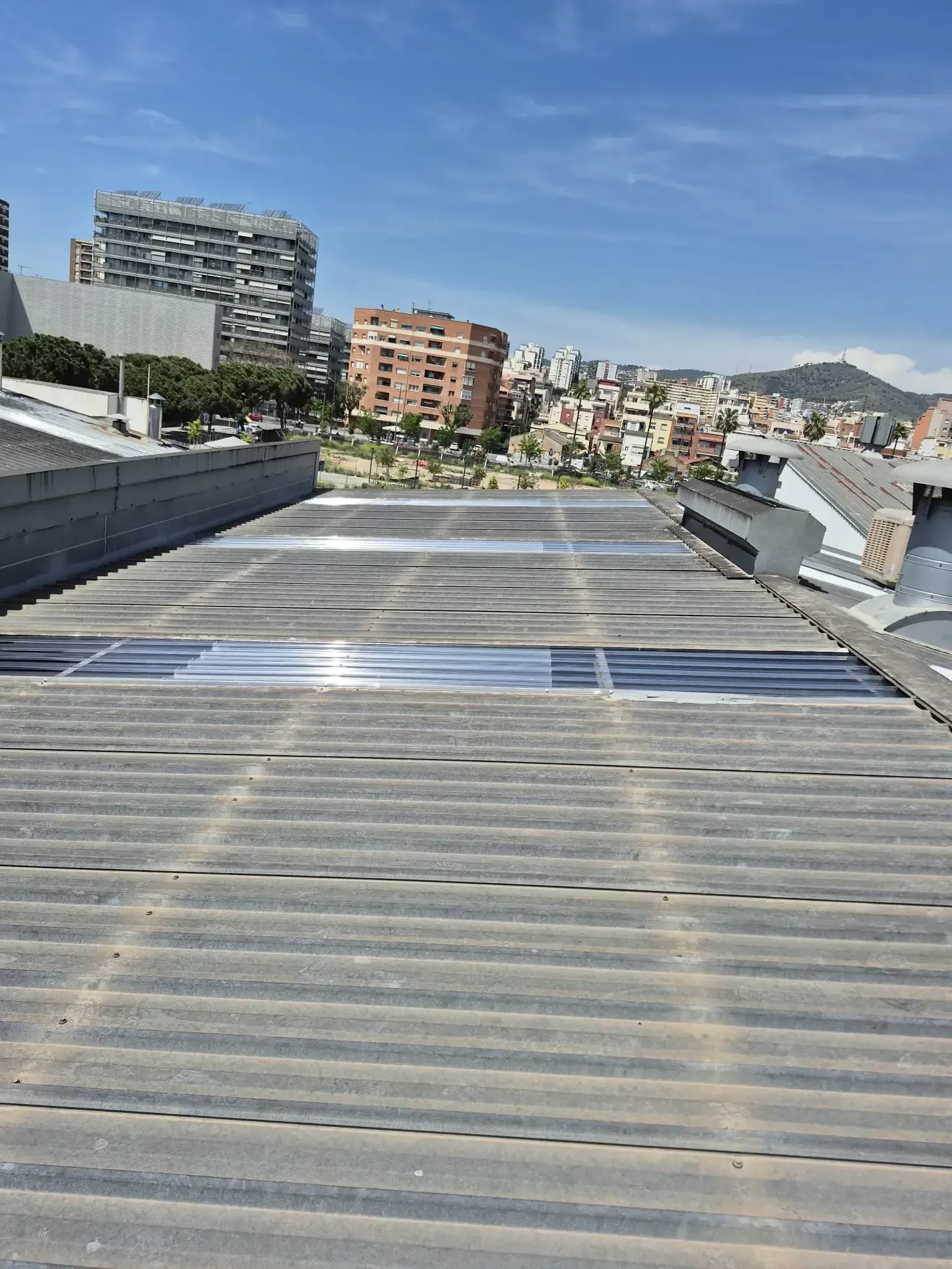 Pasarela en la azotea con paneles de metal corrugado y vistas al horizonte urbano en un día soleado