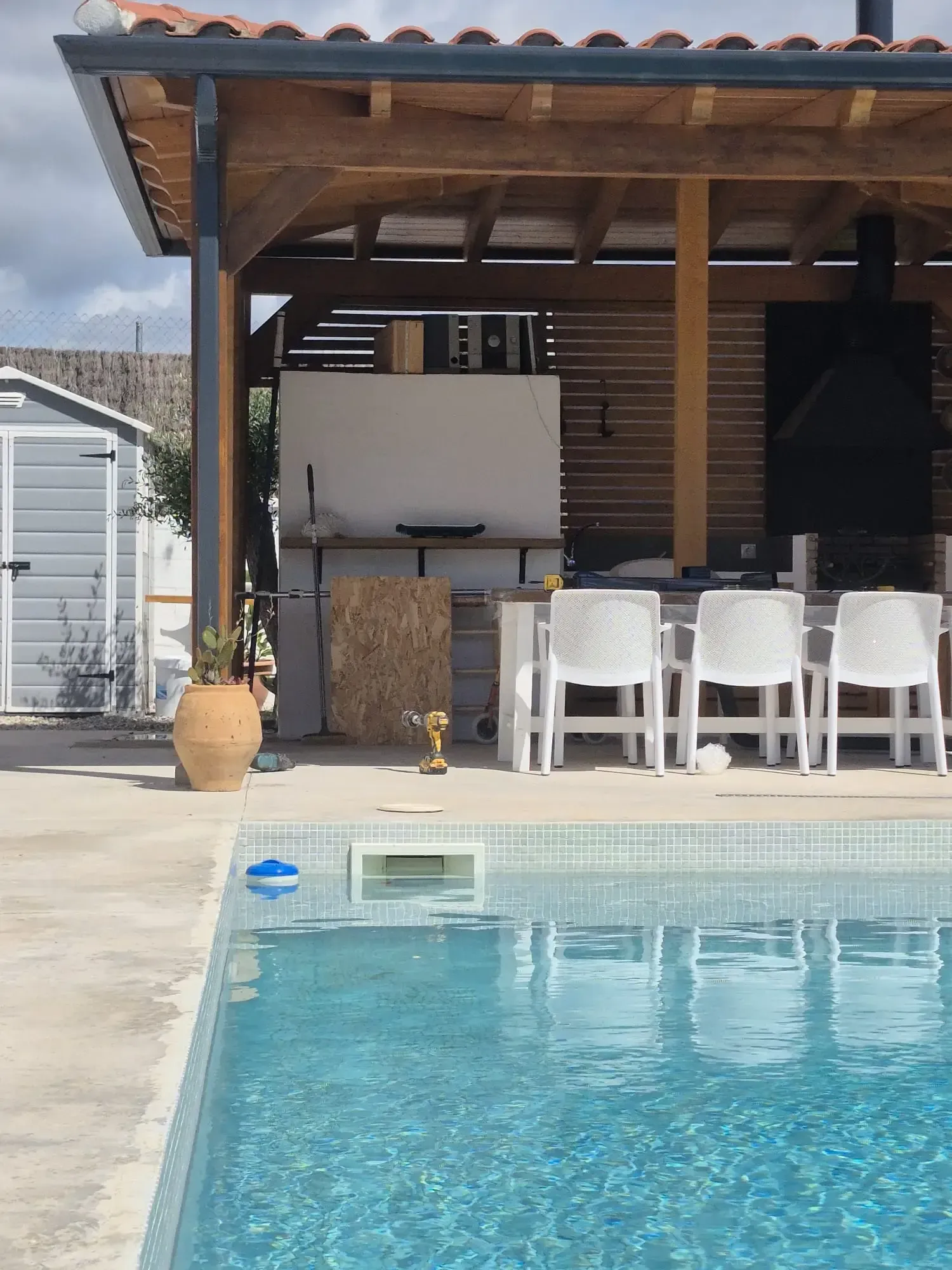 Patio junto a la piscina con taburetes de bar blancos, un techo de paja y una piscina turquesa en primer plano