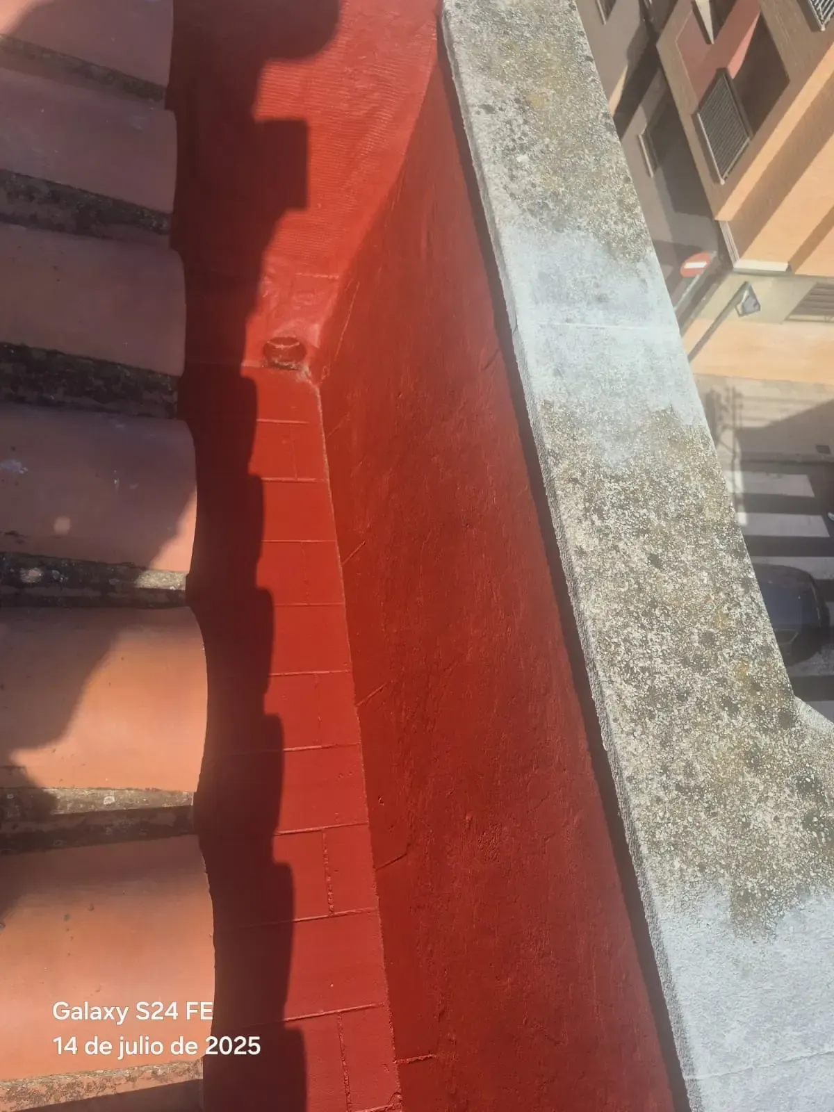 Pretil de azotea pintado de rojo, junto a un borde de hormigón y las paredes de los edificios adyacentes.