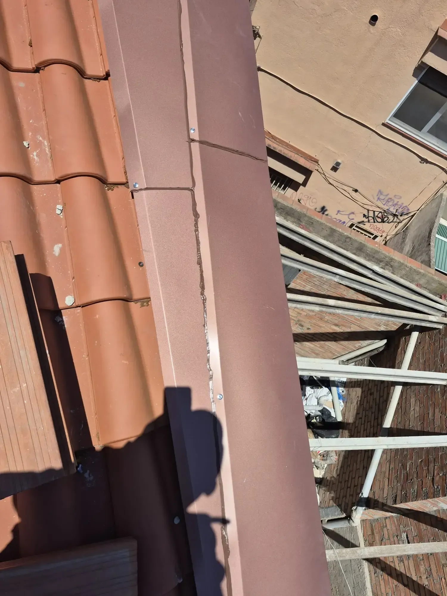 Vista inclinada de un tejado de tejas de terracota y una estructura metálica junto a la pared de un edificio beige.