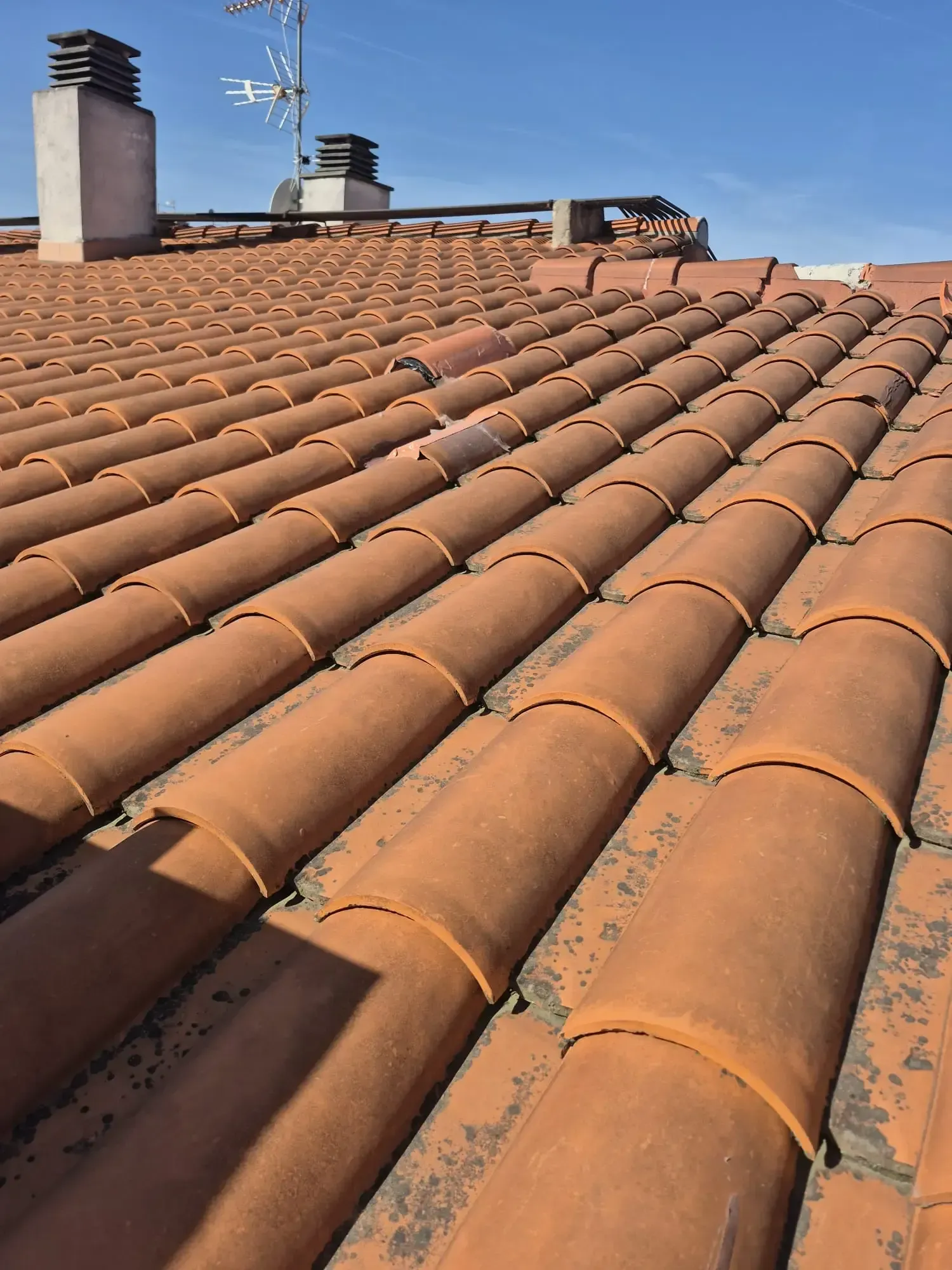 Tejas de terracota con dos chimeneas bajo un cielo azul despejado