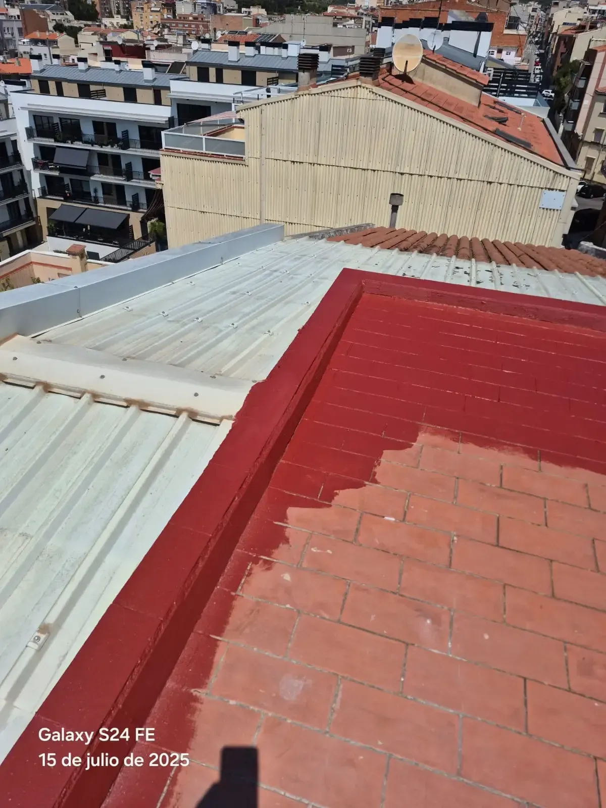 Vista desde una azotea, con tejados metálicos rojos y blancos que dominan un paisaje urbano densamente edificado.