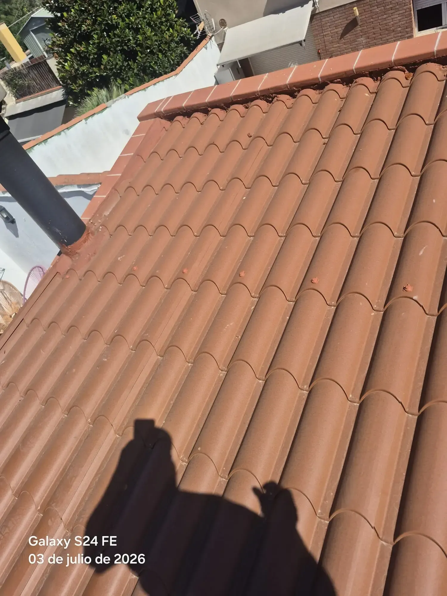 Tejado de tejas de terracota visto desde arriba, con una chimenea y sombras proyectadas en la azotea.