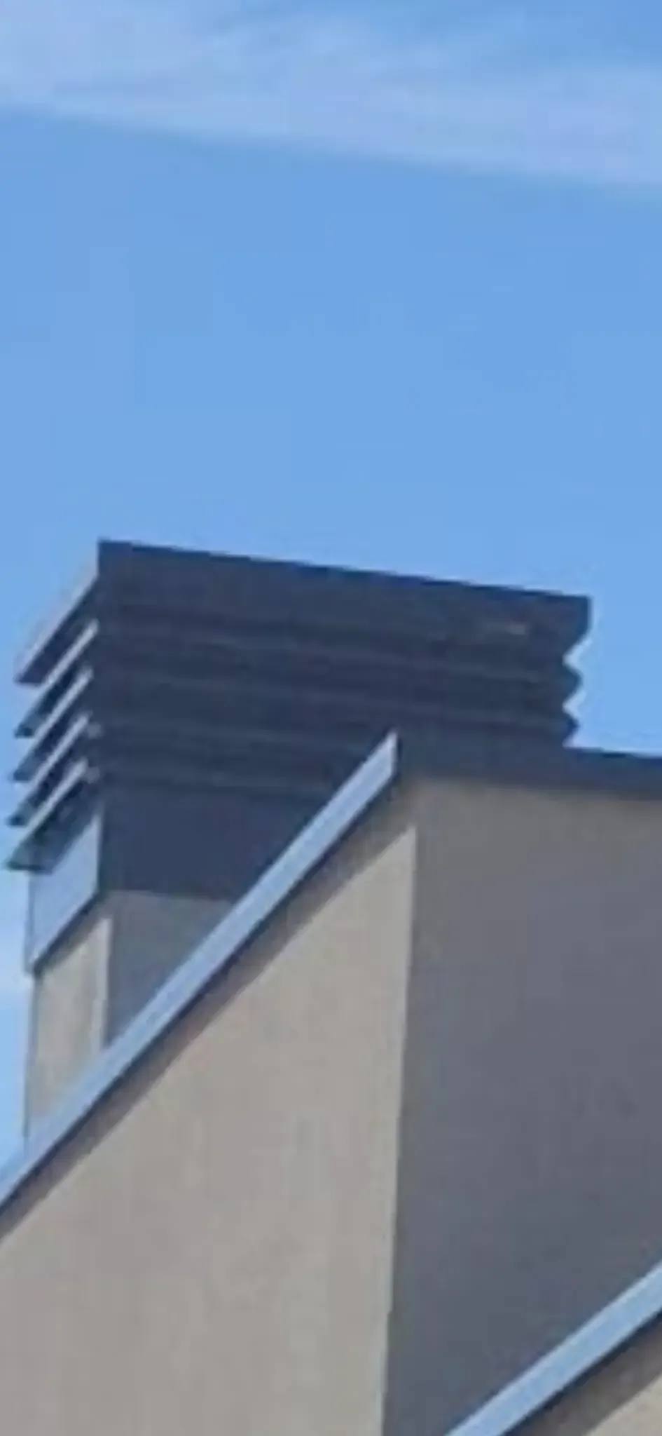 Azotea de un edificio moderno con una rejilla de ventilación de lamas oscuras frente a un cielo azul