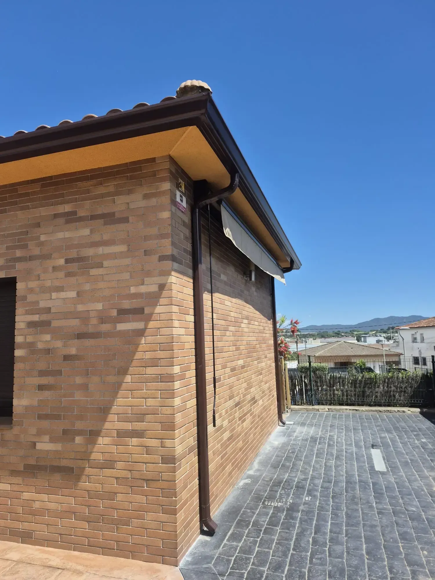 Casa de ladrillo con tejado de tejas y entrada pavimentada, bajo un cielo azul despejado