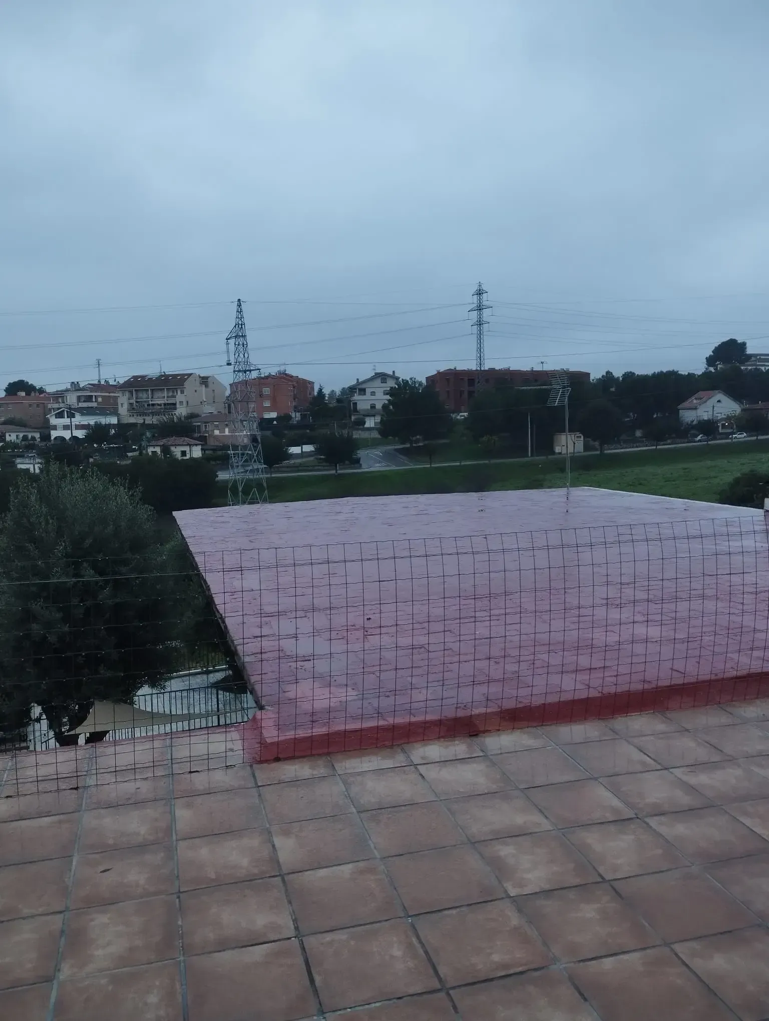 Terraza en la azotea con baldosas rosas y vistas a un barrio nublado al anochecer.