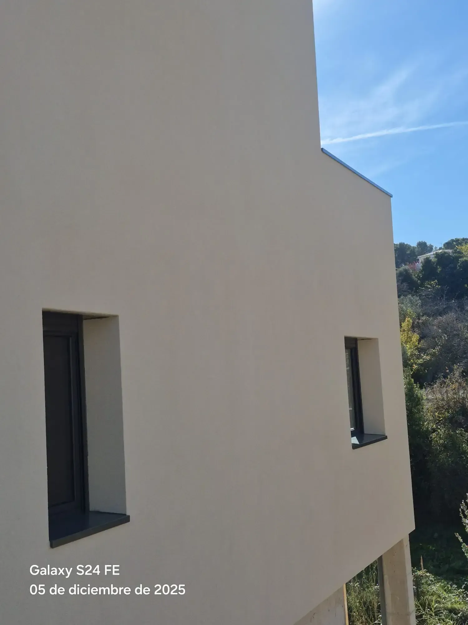 Pared blanca de estuco con dos ventanas estrechas, junto a una ladera y bajo un cielo azul