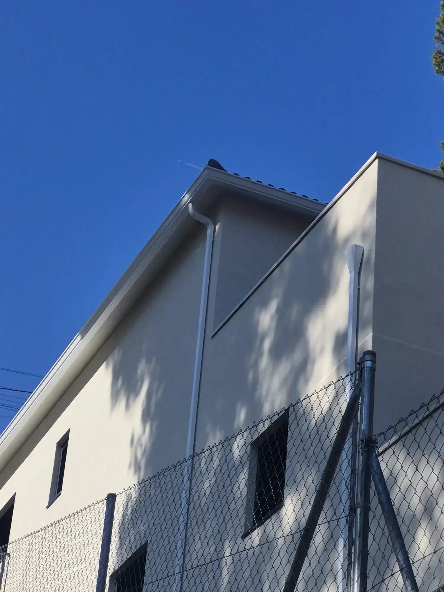 Edificio blanco con techo inclinado detrás de una cerca de alambre bajo un cielo azul despejado