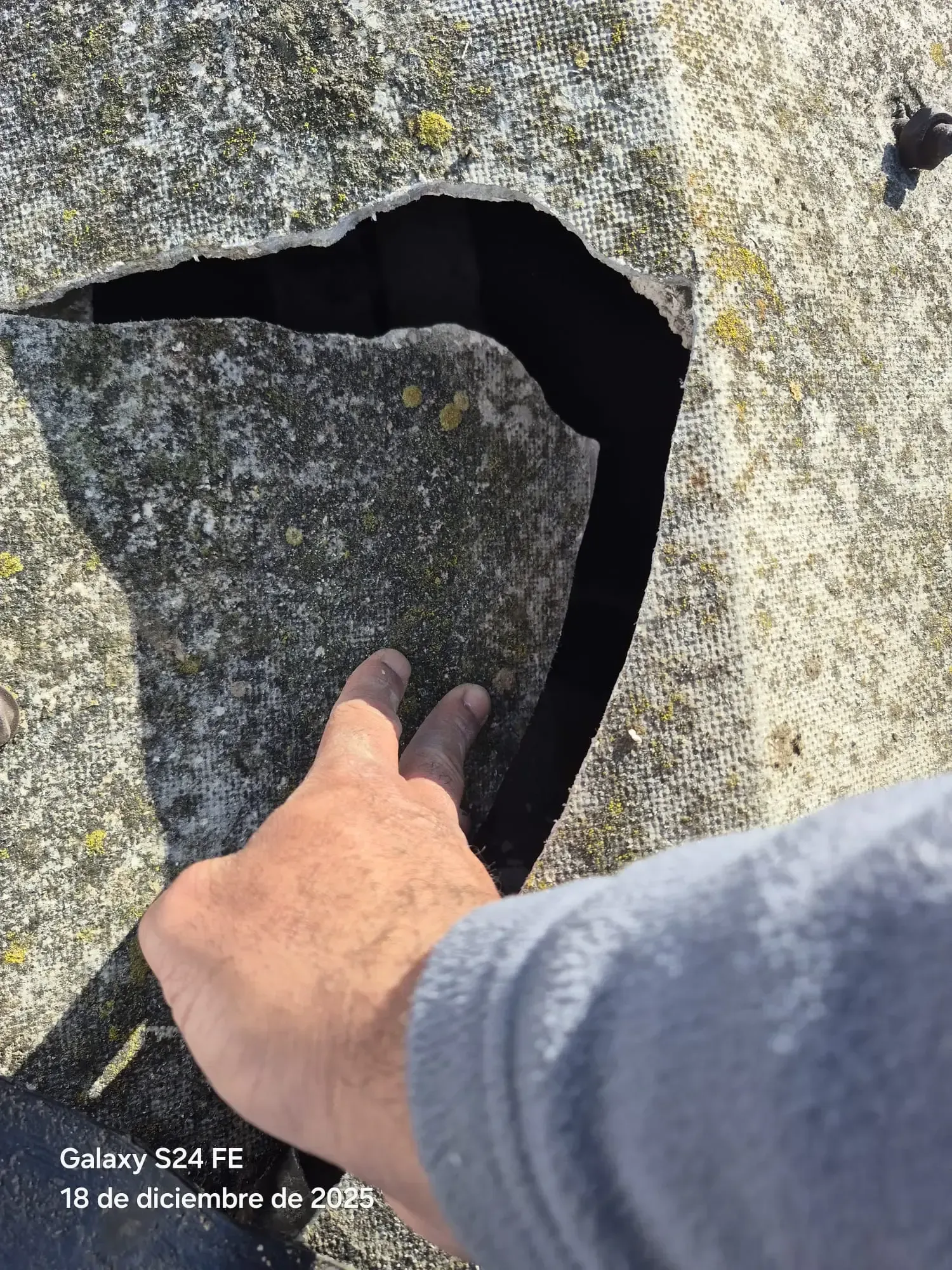 Una mano señala una grieta oscura en la superficie erosionada de una roca.