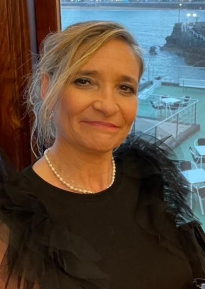 Una mujer que lleva un top negro y un collar de perlas sonríe para la cámara.