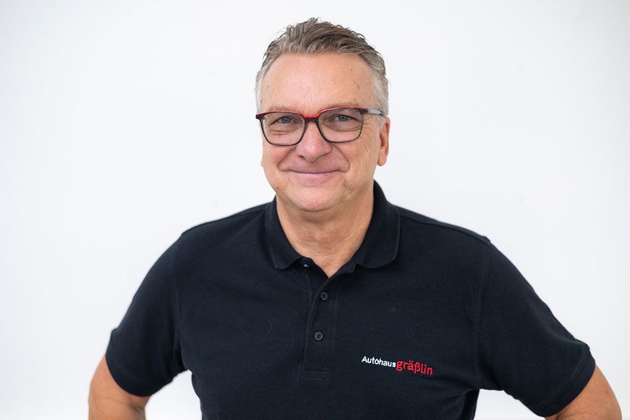 Ein Mann mit Brille und schwarzem Poloshirt lächelt in die Kamera.