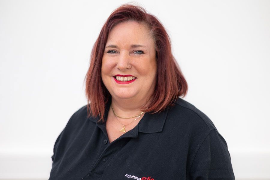 Eine Frau mit roten Haaren trägt ein schwarzes Poloshirt und lächelt.