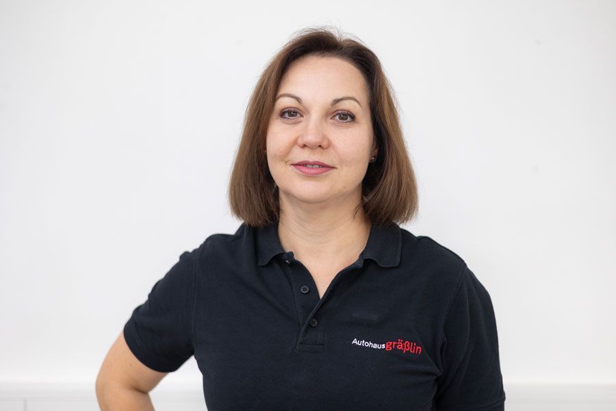 Eine Frau in einem schwarzen Poloshirt steht vor einer weißen Wand.