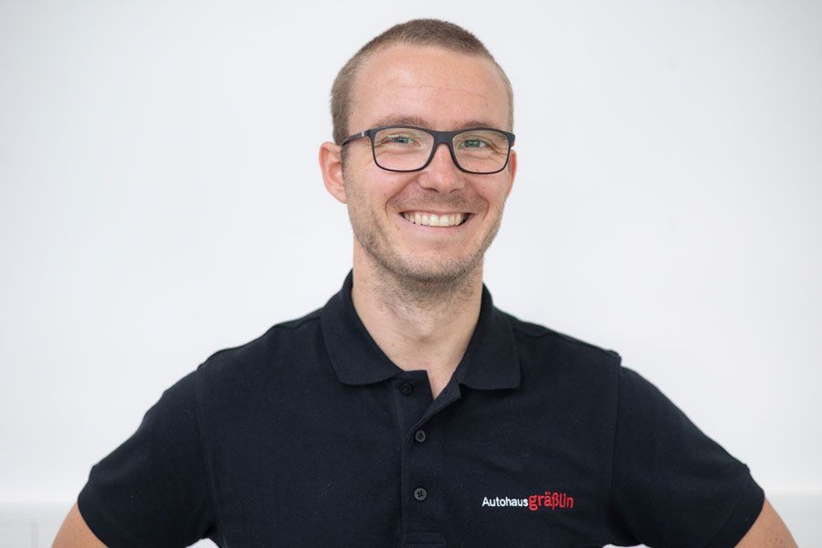 Ein Mann mit Brille und schwarzem Poloshirt lächelt.