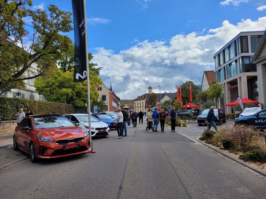 Eine Gruppe von Menschen geht eine Straße entlang . Am Straßenrand sind Autos geparkt.