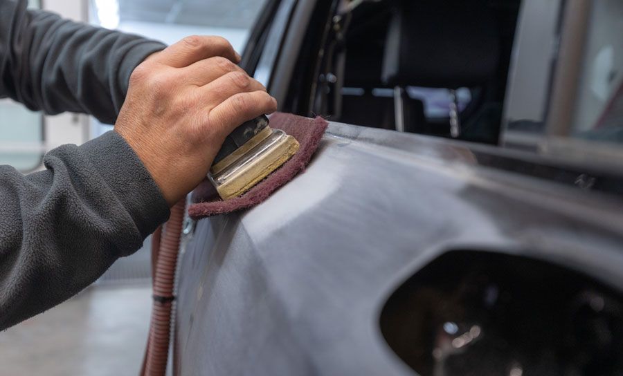 Ein Mann schleift die Seite eines Autos mit Schleifpapier ab.