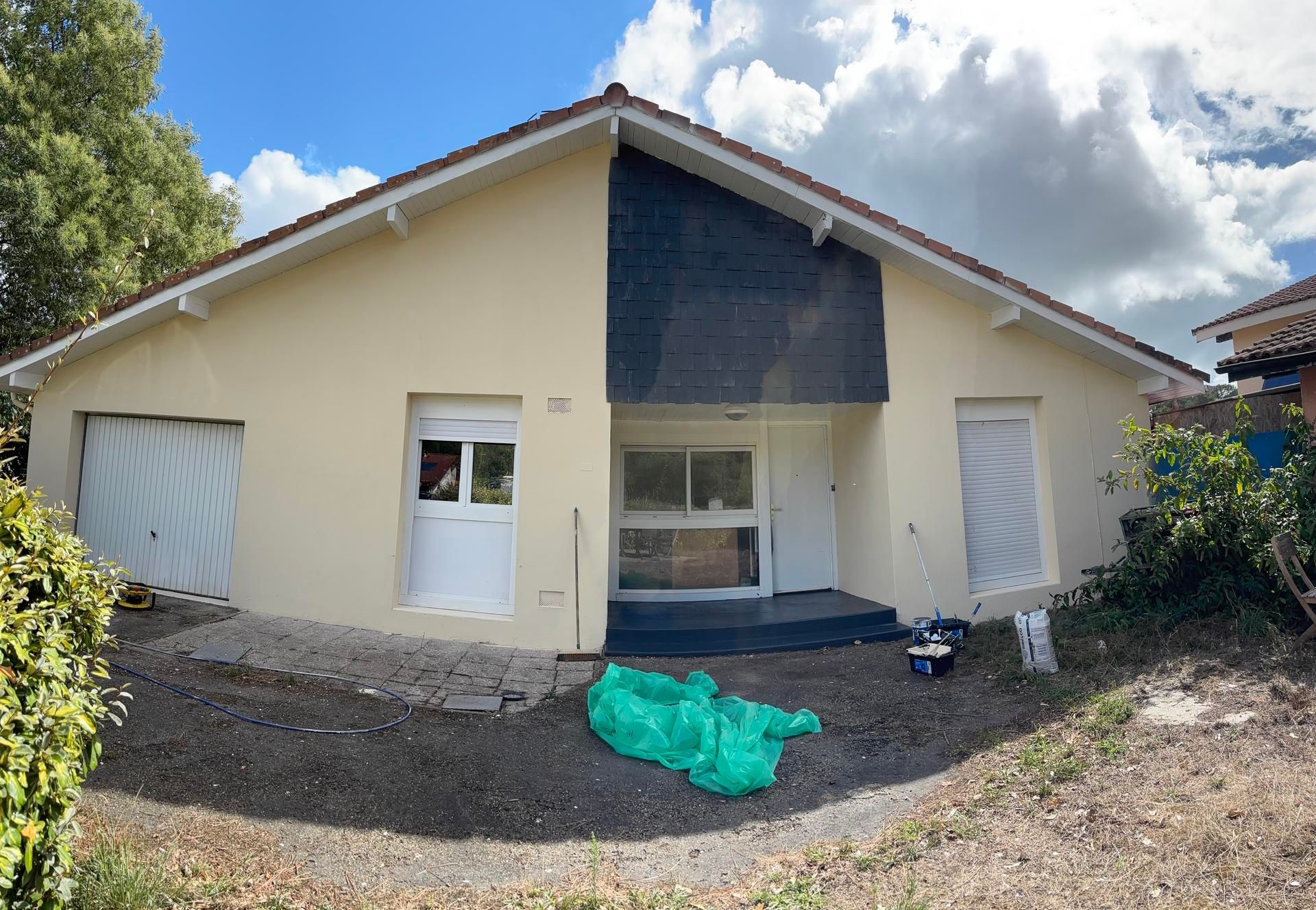 Maison beige avec portes blanches et une touche de gris foncé au-dessus de l'entrée, par temps nuageux.