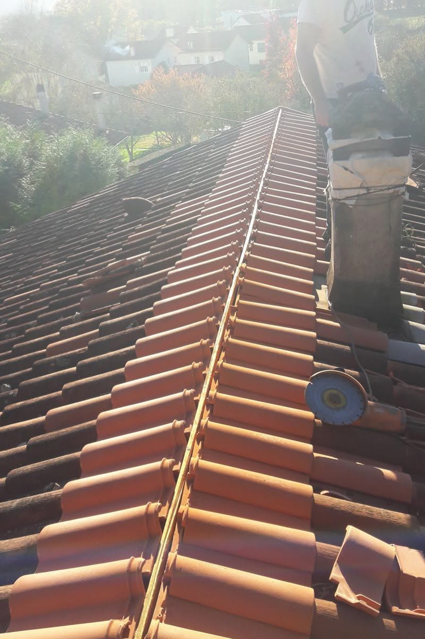 Couvreur sur un toit de tuiles en terre cuite, près d'une cheminée. Journée nuageuse avec vue.