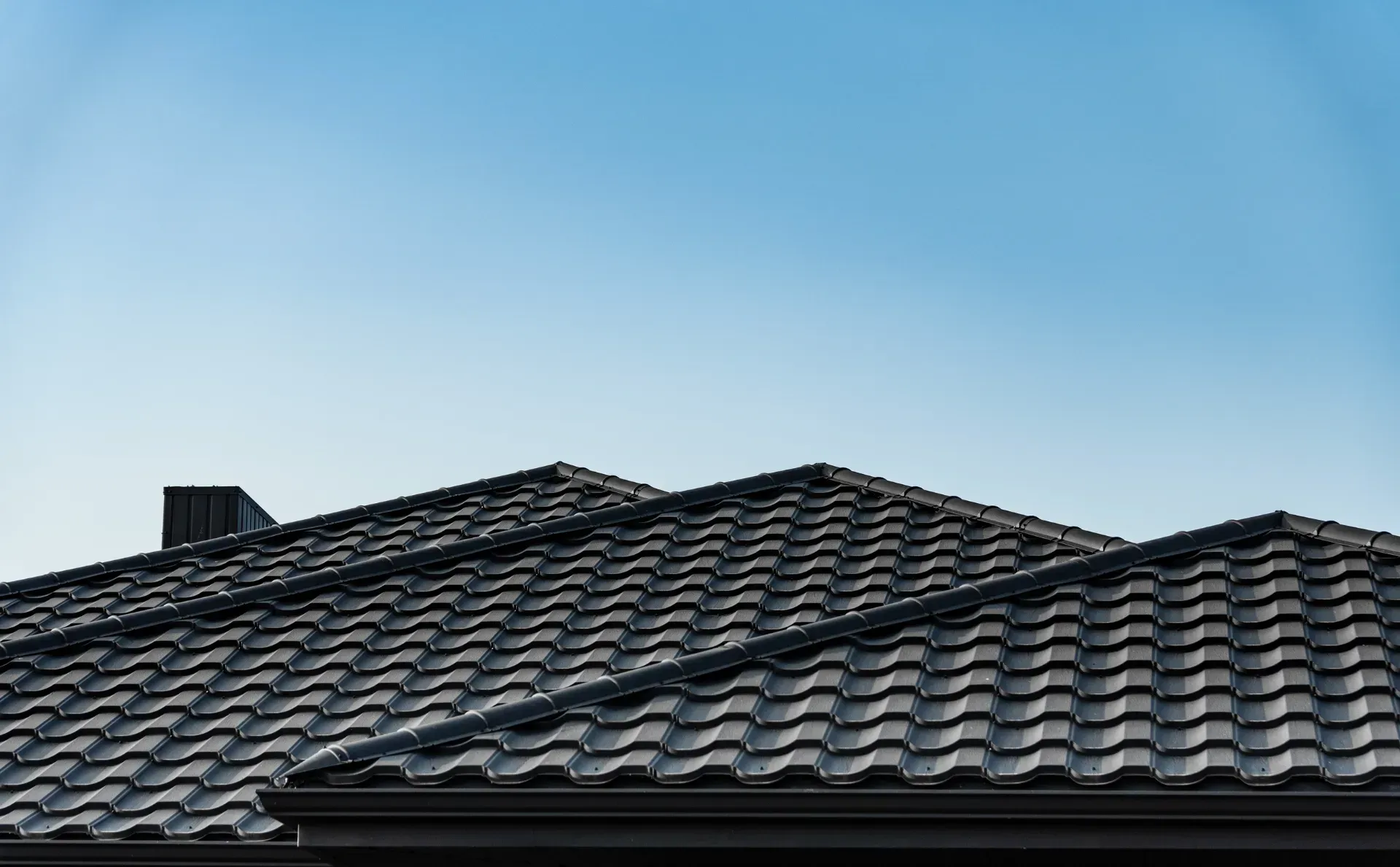 Un primer plano de un techo de tejas negras con un cielo azul de fondo.