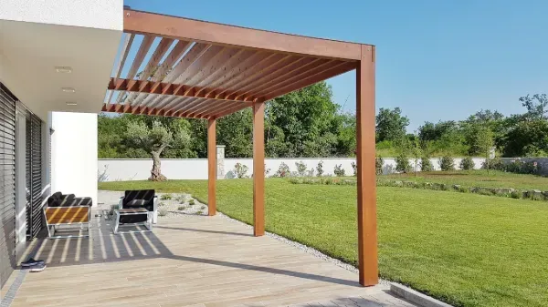 Una pérgola de madera está situada encima de un patio al lado de una casa.