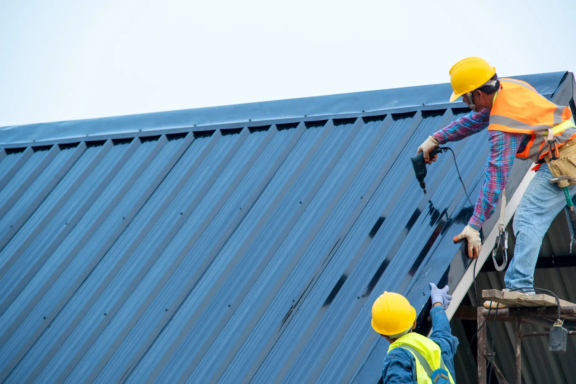 Dos obreros de la construcción están trabajando en un tejado azul.
