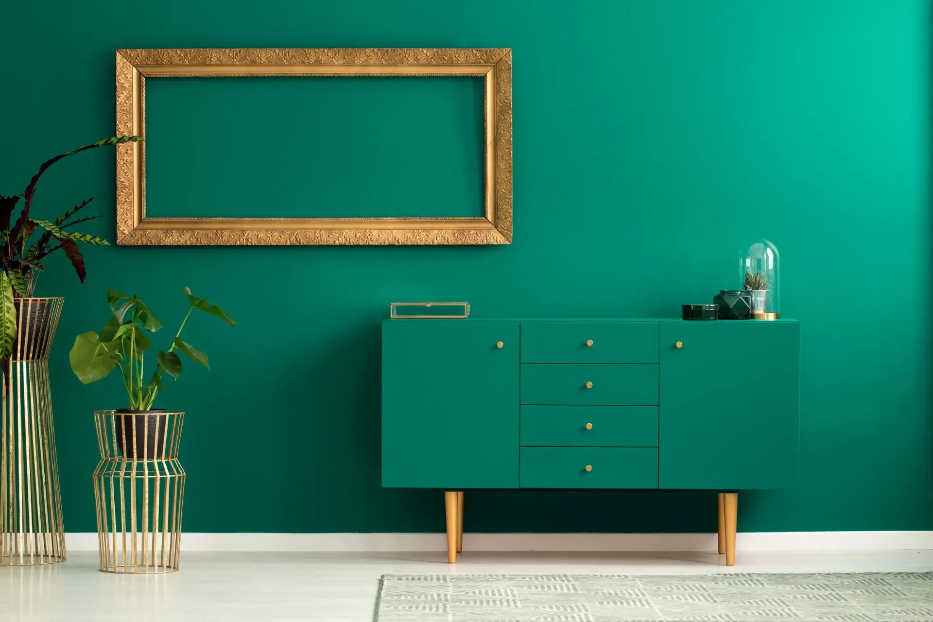 Una sala de estar con paredes verdes, una cómoda verde y un marco dorado colgado en la pared.