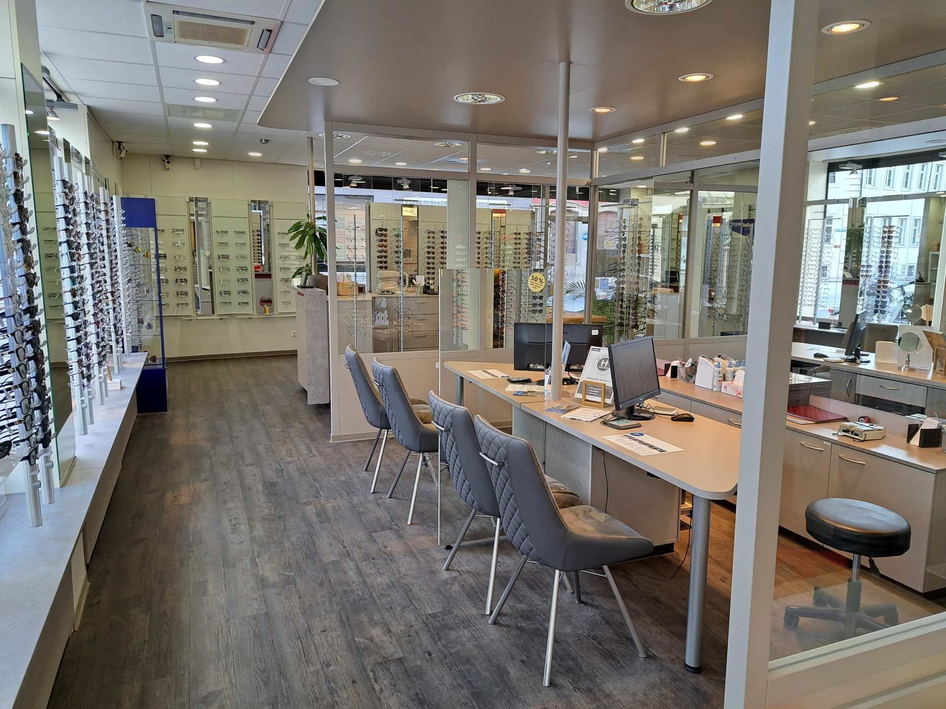 Eine Hand wählt in einem Optikergeschäft eine dünngerahmte Brille aus einem Ausstellungsständer aus.
