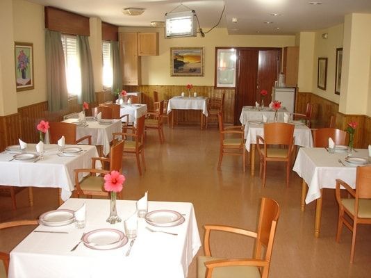 Un comedor con mesas y sillas preparadas para comer.