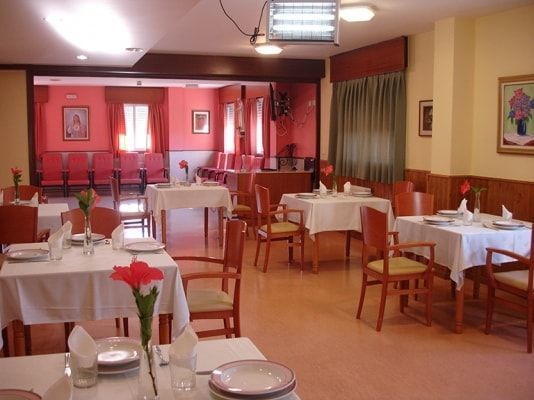 Un comedor con mesas y sillas preparadas para comer.