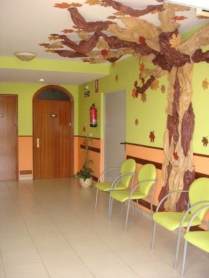 Un pasillo con sillas verdes y un árbol en la pared.