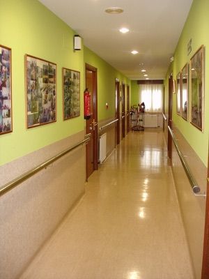 Un largo pasillo con paredes verdes y un extintor de incendios en la pared.