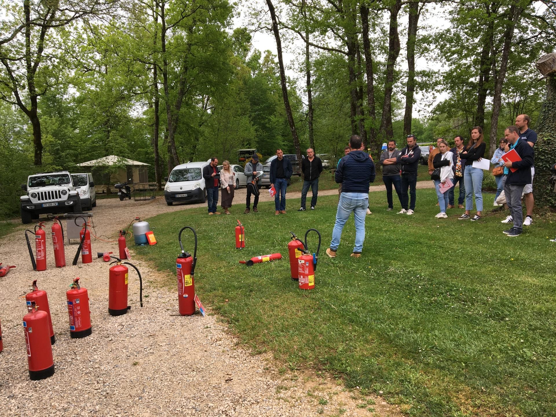 Groupe d'apprentissage de la sécurité incendie en extérieur, avec extincteurs disposés au sol et un formateur qui parle.