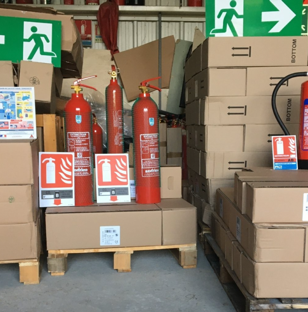 Extincteurs et cartons sur palettes dans un entrepôt.