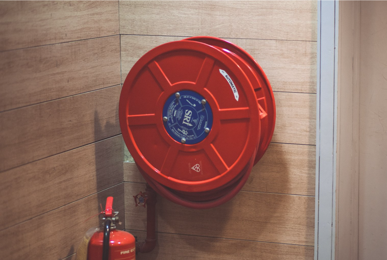Enrouleur de tuyau d'incendie avec un extincteur rouge en dessous.