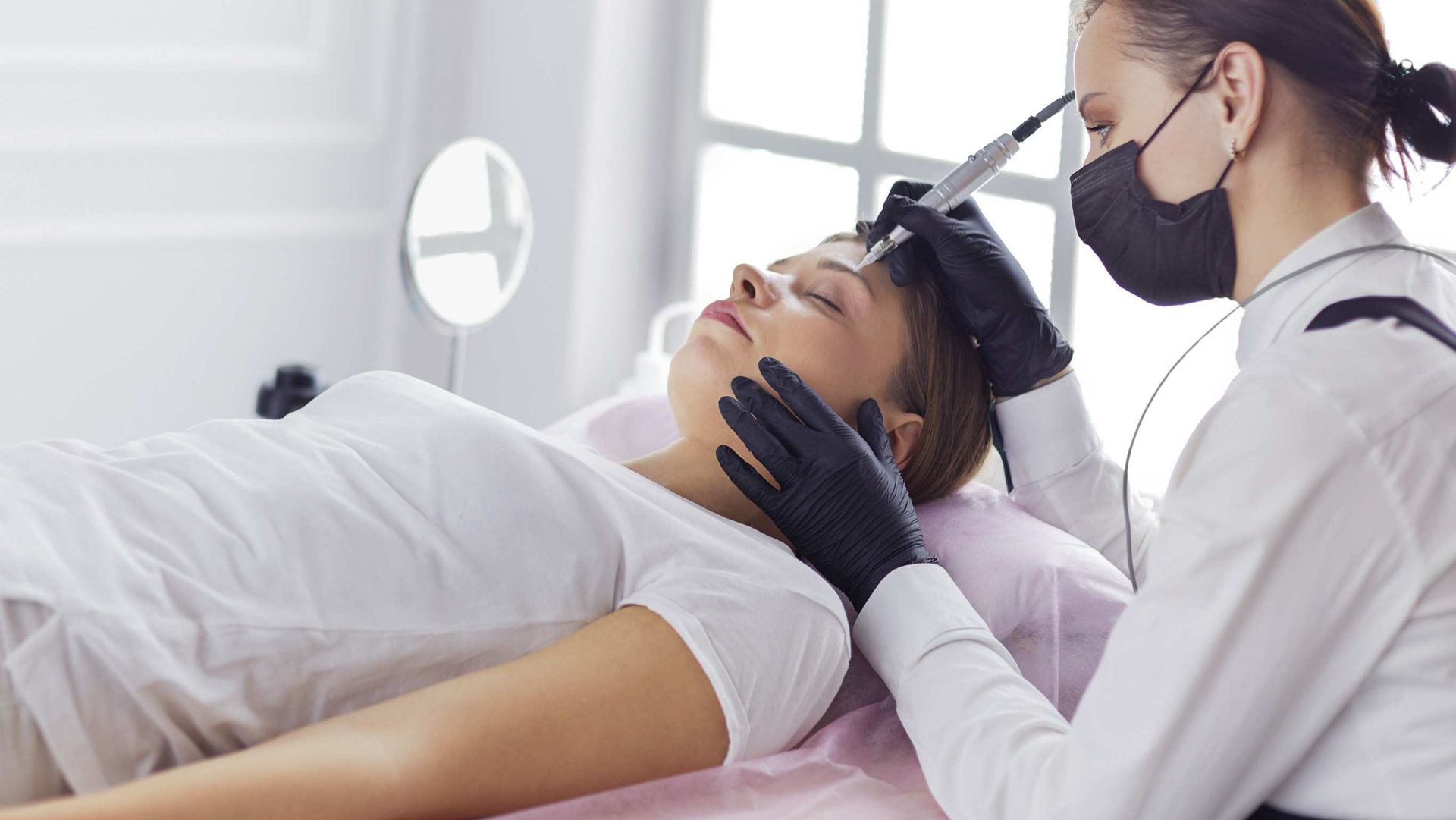 Una mujer está acostada en una cama haciéndose un tatuaje en las cejas.