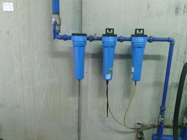 Tres filtros de agua azules están conectados a una tubería en una pared.