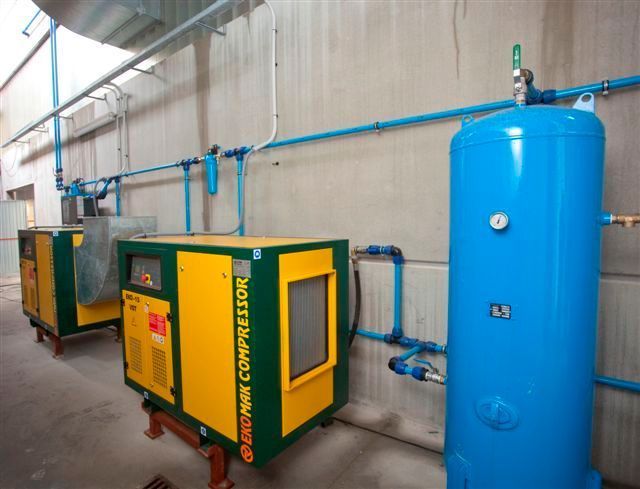 Un compresor de aire amarillo y verde está al lado de un tanque azul.